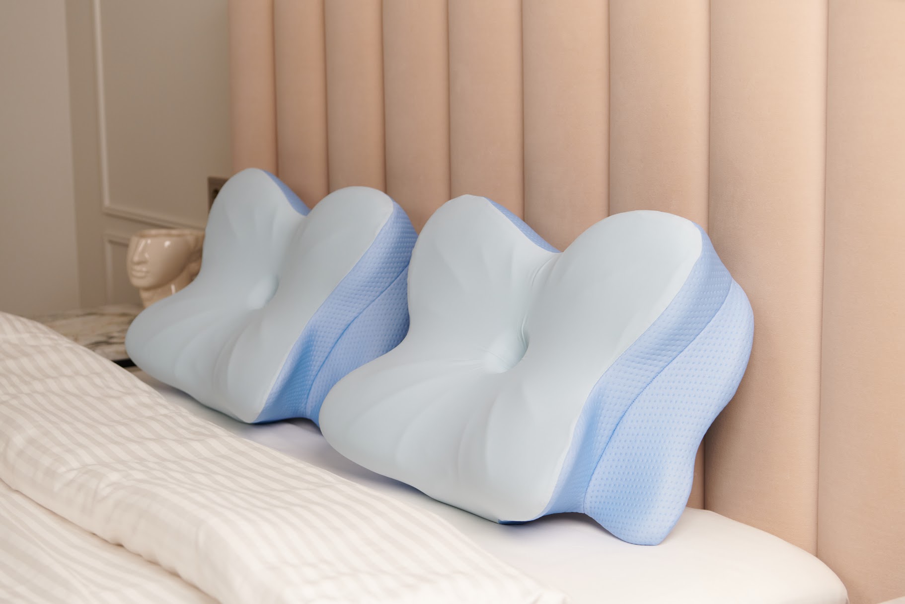 Two pale-blue and white Derila Ergo contour pillows against a beige upholstered headboard.
